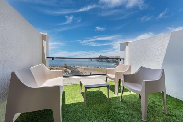 A balcony with artificial grass, two white chairs, and a small table.
