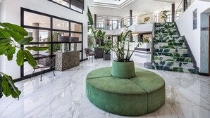 A spacious lobby with a green seating area, a staircase with a tropical design, and a large skylight. - Occidental Roca Negra – Adults Only (Agaete)