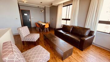 A modern living room with a brown leather sofa, patterned armchairs, and a dining table with orange chairs.