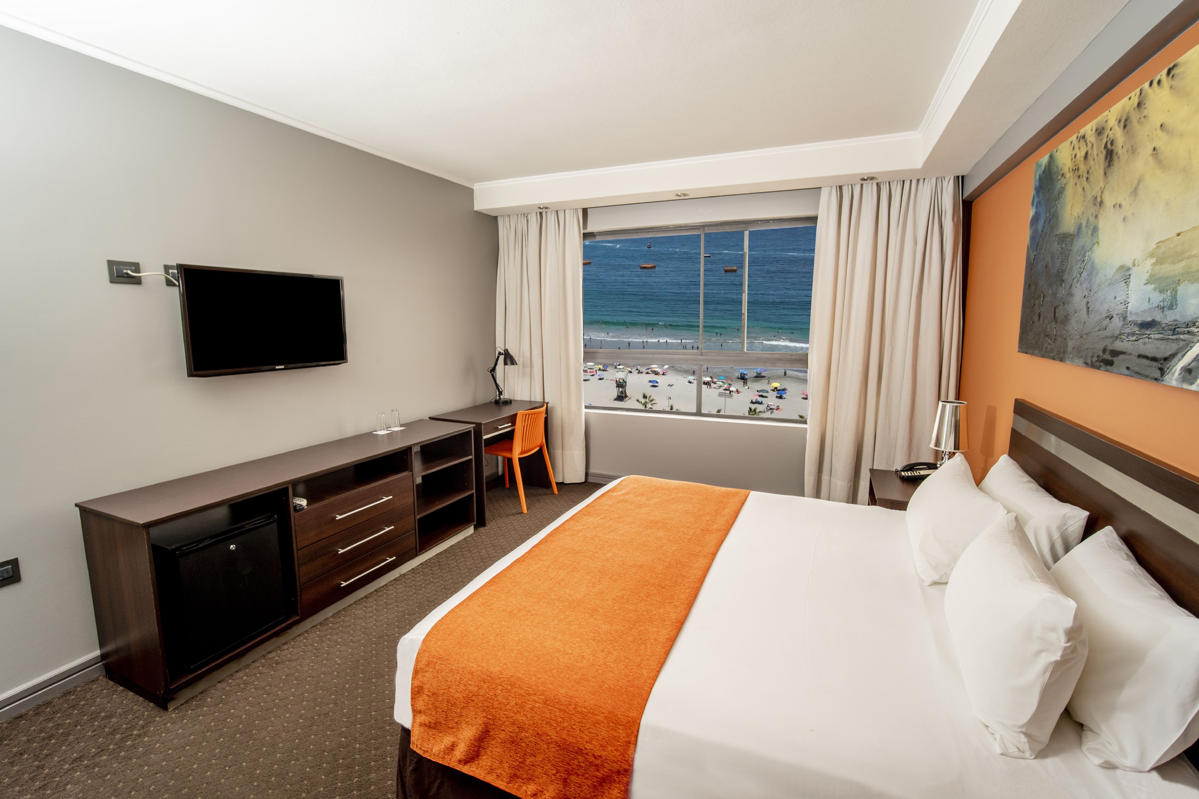 Een hotelkamer met een bed, bureau, televisie en uitzicht op het strand.