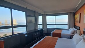 Habitación de hotel con dos camas, un ventanal con vistas a la ciudad, un televisor y un cuadro en la pared.