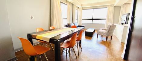Una sala de estar moderna con comedor, ventanas amplias y un televisor de pantalla plana.