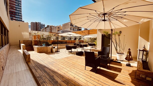 Una terraza en la azotea con suelo de madera, asientos exteriores y sombrillas.