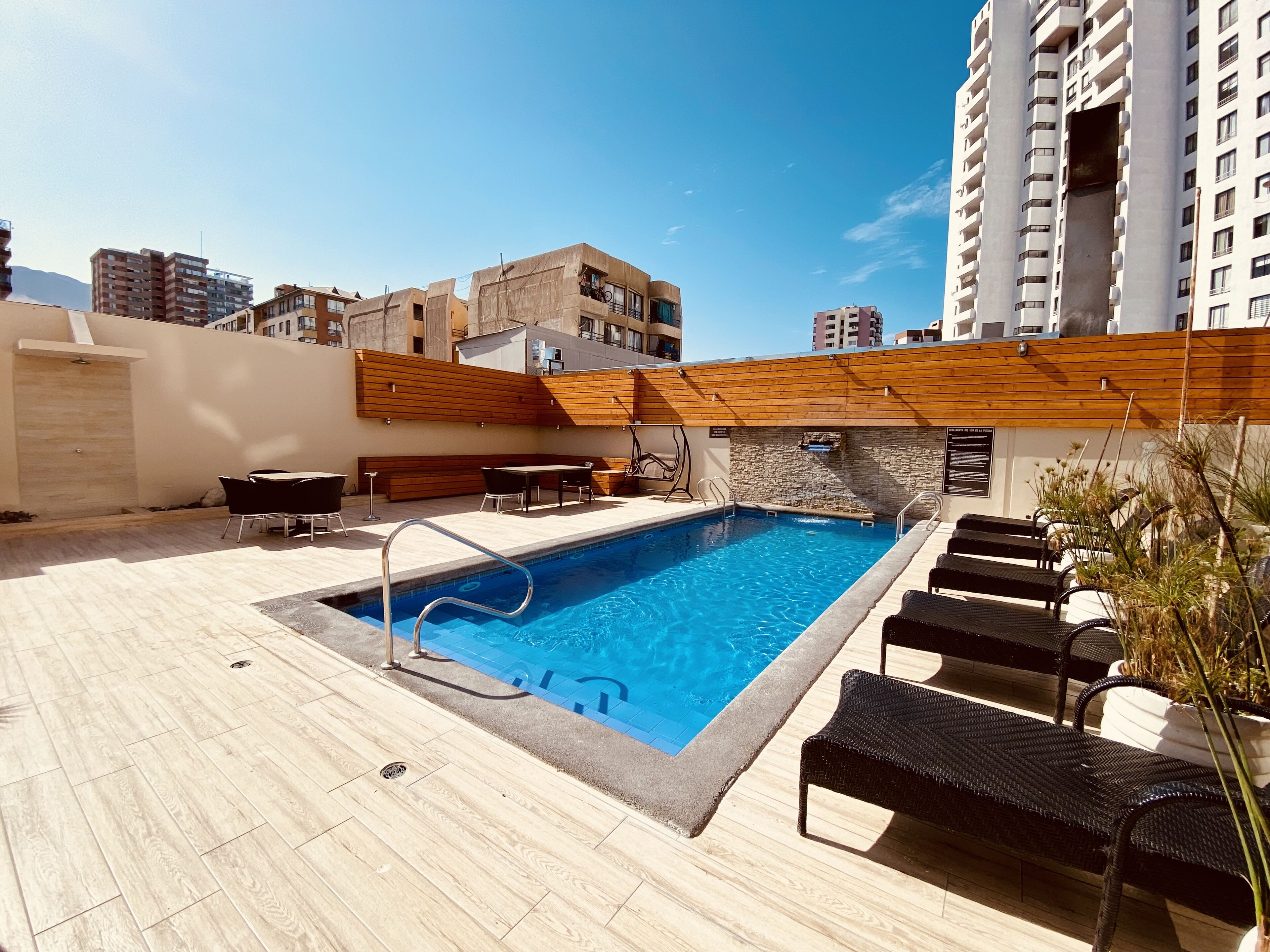 A rooftop pool area with a pool, lounge chairs, and a wooden deck.