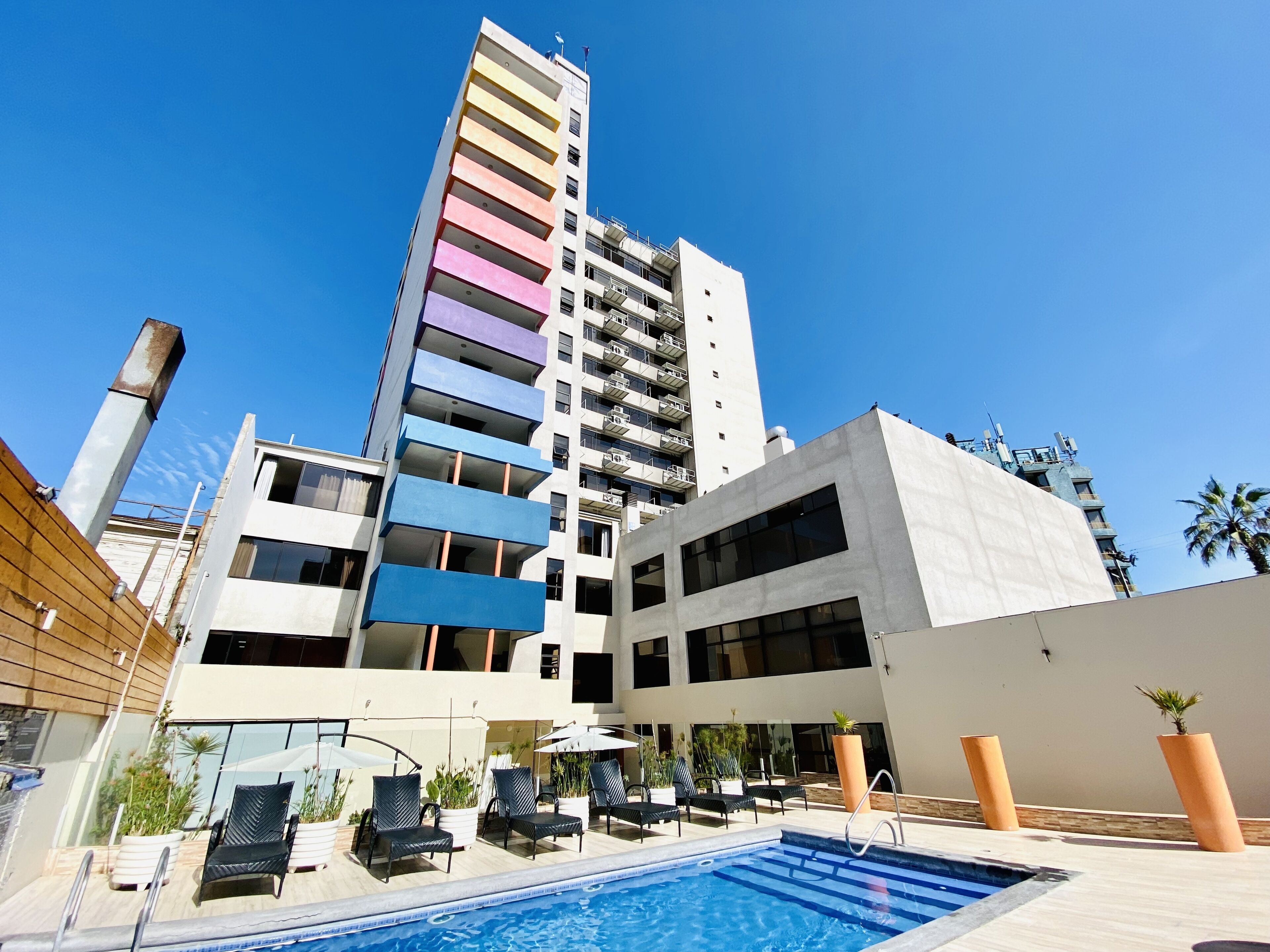 A modern hotel with a rooftop pool, multiple balconies, and a clear blue sky.