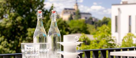 A balcony with a table set for tea, featuring two bottles and several cups.