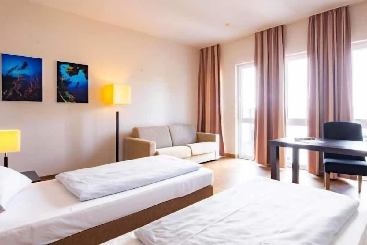 A hotel room with two beds, a desk with a chair, a television, and two paintings on the wall.