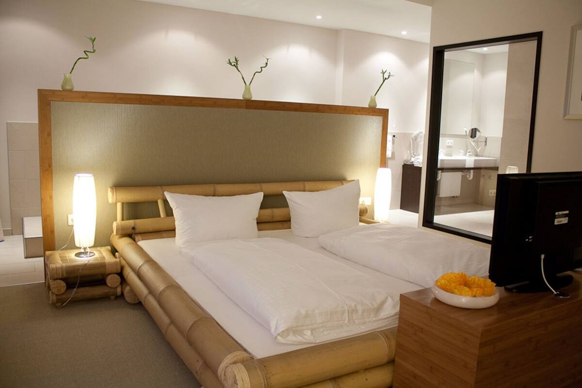 A hotel room with a large bed, bedside lamps, a wooden headboard, a mirror, and a television.