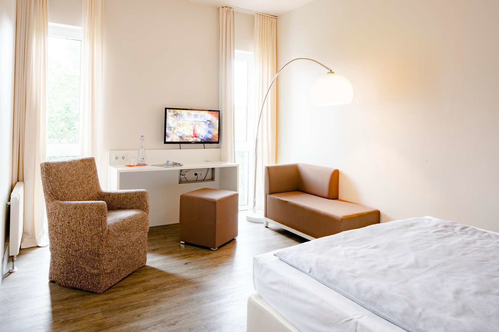 A hotel room with a bed, a sofa, a chair, a desk with a TV, and a lamp.