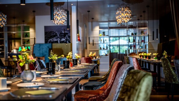 A restaurant with long tables, chairs, and hanging lights. - Friendly City Hotel Oktopus (Siegburg)