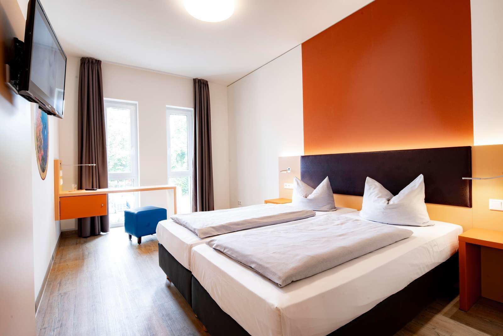 A modern hotel room with two beds, a desk, and a TV.