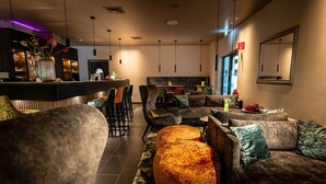 A modern lounge area with sofas, a round ottoman, and a bar counter. - Friendly City Hotel Oktopus (Siegburg)