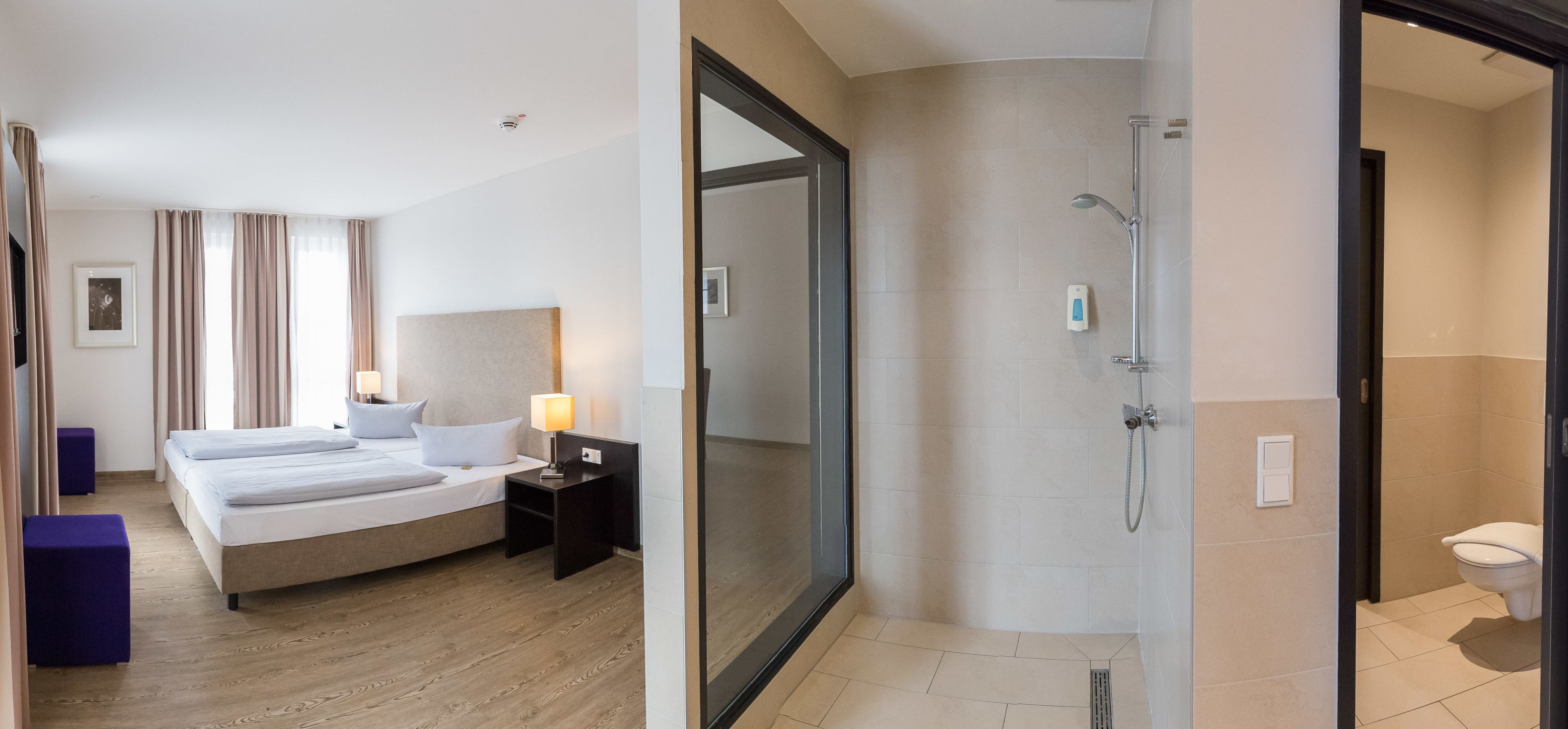 A hotel room with a bed, bedside tables, a lamp, and a shower area.