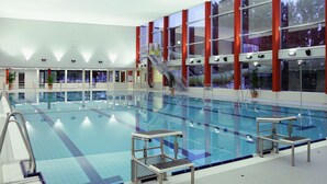 An indoor swimming pool with multiple lanes, a diving platform, and a staircase leading to an upper level. - Friendly City Hotel Oktopus (Siegburg)