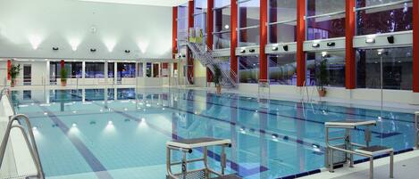 An indoor swimming pool with multiple lanes, a diving platform, and a staircase leading to an upper level.