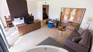 A modern hotel room with a large bed, a sofa, a desk, a TV, a mirror, and a bathtub. - Friendly City Hotel Oktopus (Siegburg)