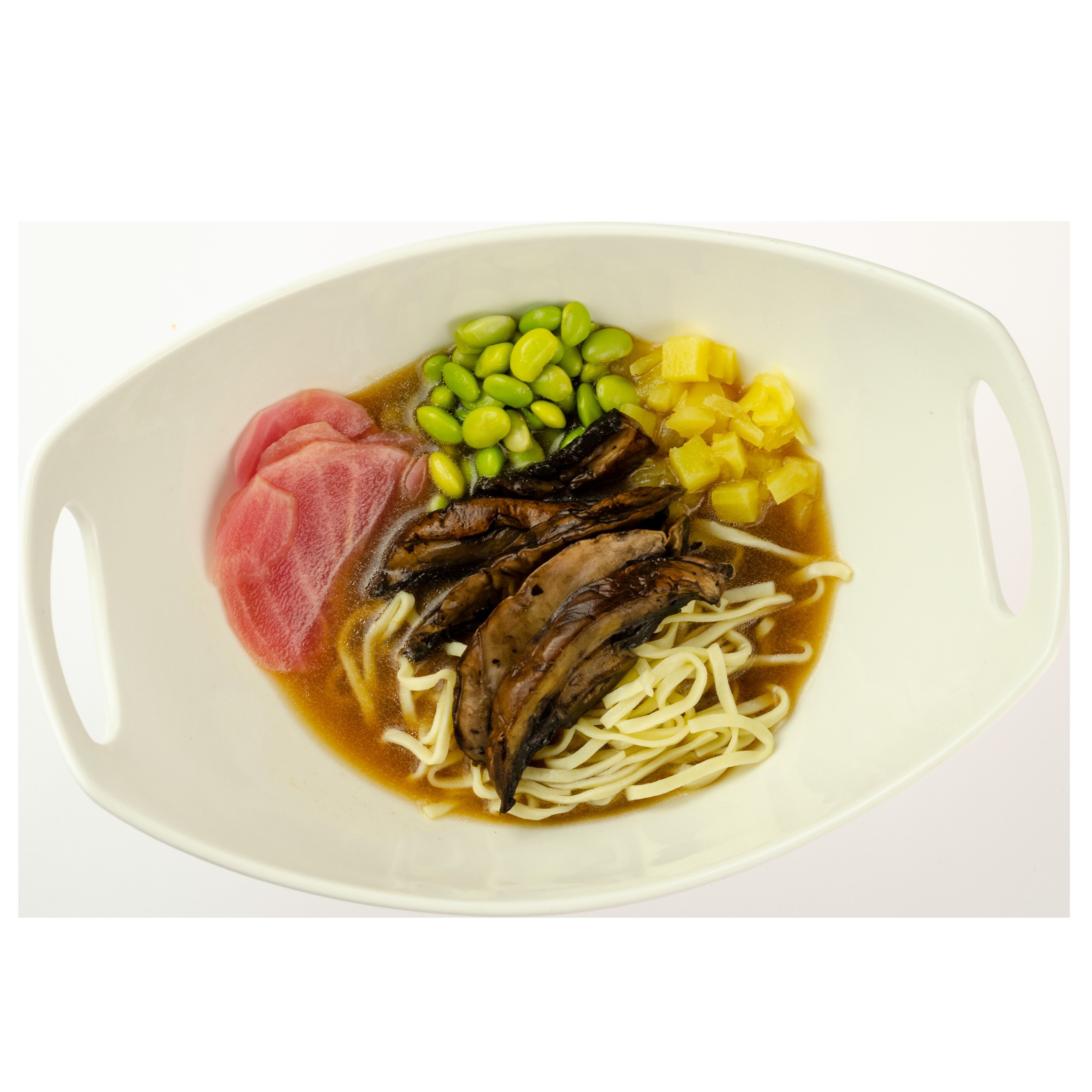 A bowl of ramen with toppings including green edamame, pineapple chunks, mushrooms, and a slice of pink meat.