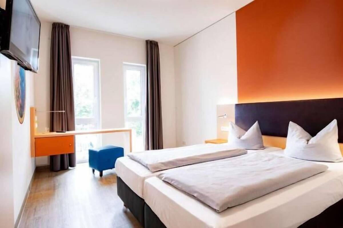 A hotel room with two beds, a desk, a chair, and a TV.