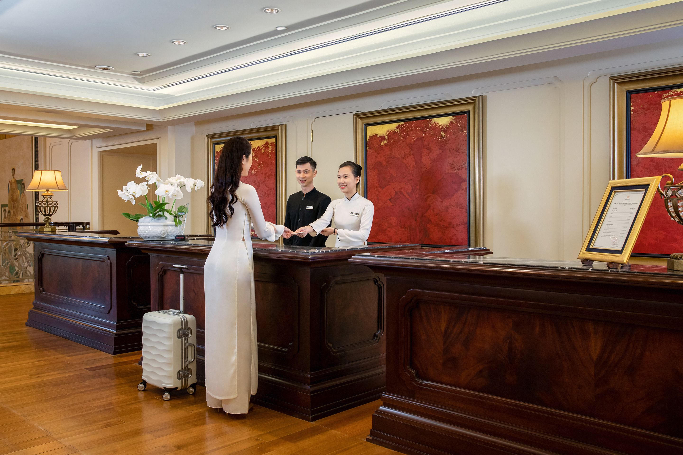 A reception area with a wooden desk, a white vase with flowers, and a framed certificate on the desk.