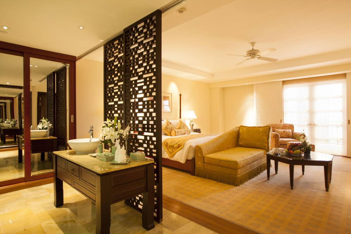 A hotel room with a large bed, a sofa, a coffee table, and a bathroom with a sink and mirror.
