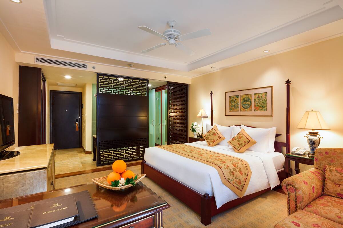 A hotel room with a large bed, a desk with a computer, a chair, and a wall-mounted TV.