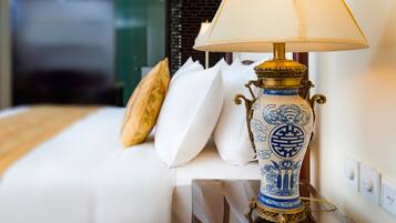 A bed with white bedding, a decorative vase lamp, and a wall with a power outlet.