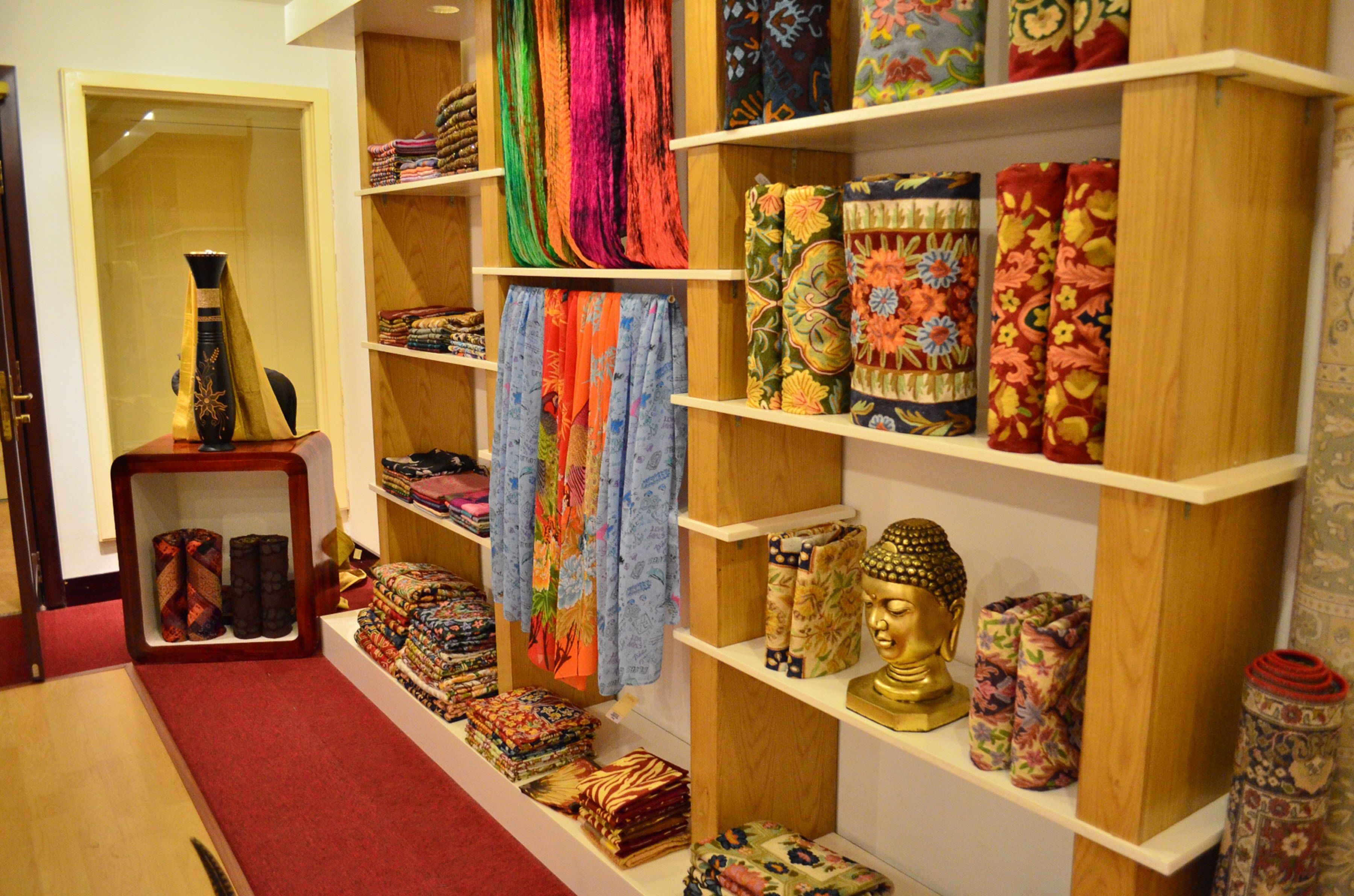 A store with shelves of colorful fabrics and a Buddha statue.