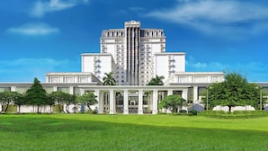 A large, white, multi-story building with a central tower, surrounded by a well-maintained lawn and trees. - Indochine Palace (Hue)