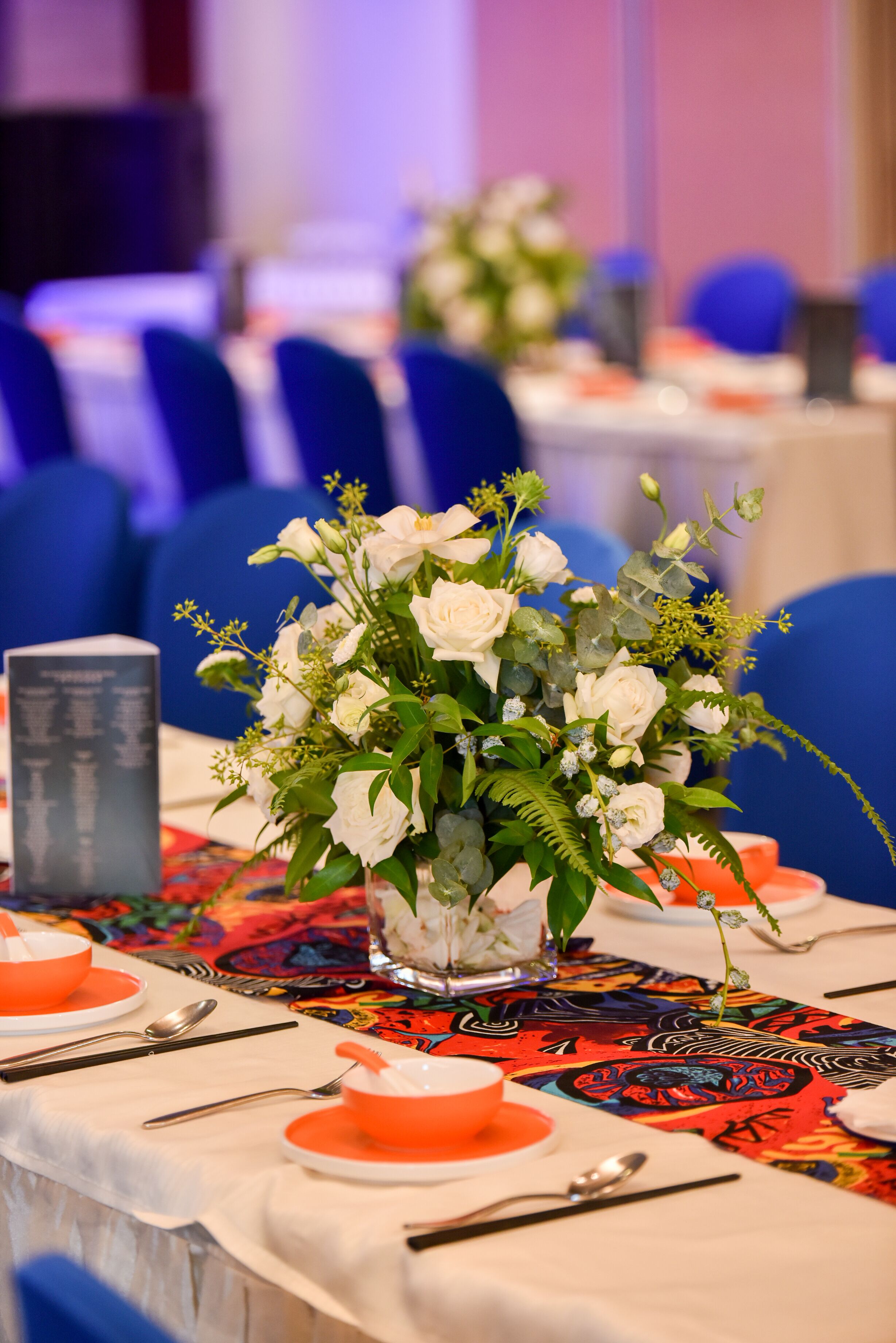 Ein Tisch ist gedeckt mit einer Vase voller weißer Blumen, einem Menüständer und Geschirr in Orange und Weiß.