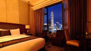 A hotel room with a large bed, a desk, a chair, and a view of a cityscape at night. - Asta Hotel (Shenzhen)
