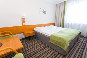 A hotel room with a bed, a desk, a chair, a lamp, and a window with curtains.