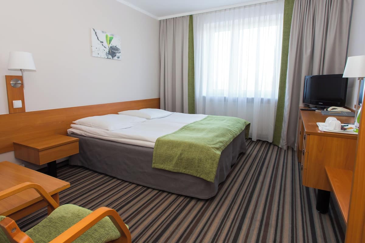 A hotel room with a bed, a desk, a chair, a television, and a window with curtains.