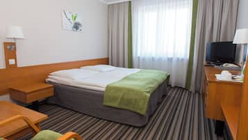 Una habitación de hotel con una cama, un escritorio, una silla, un televisor y una ventana con cortinas.