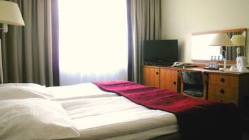 Ein Hotelzimmer mit einem Bett, einem Fernseher, einem Schreibtisch mit Lampe und einer Kaffeemaschine.