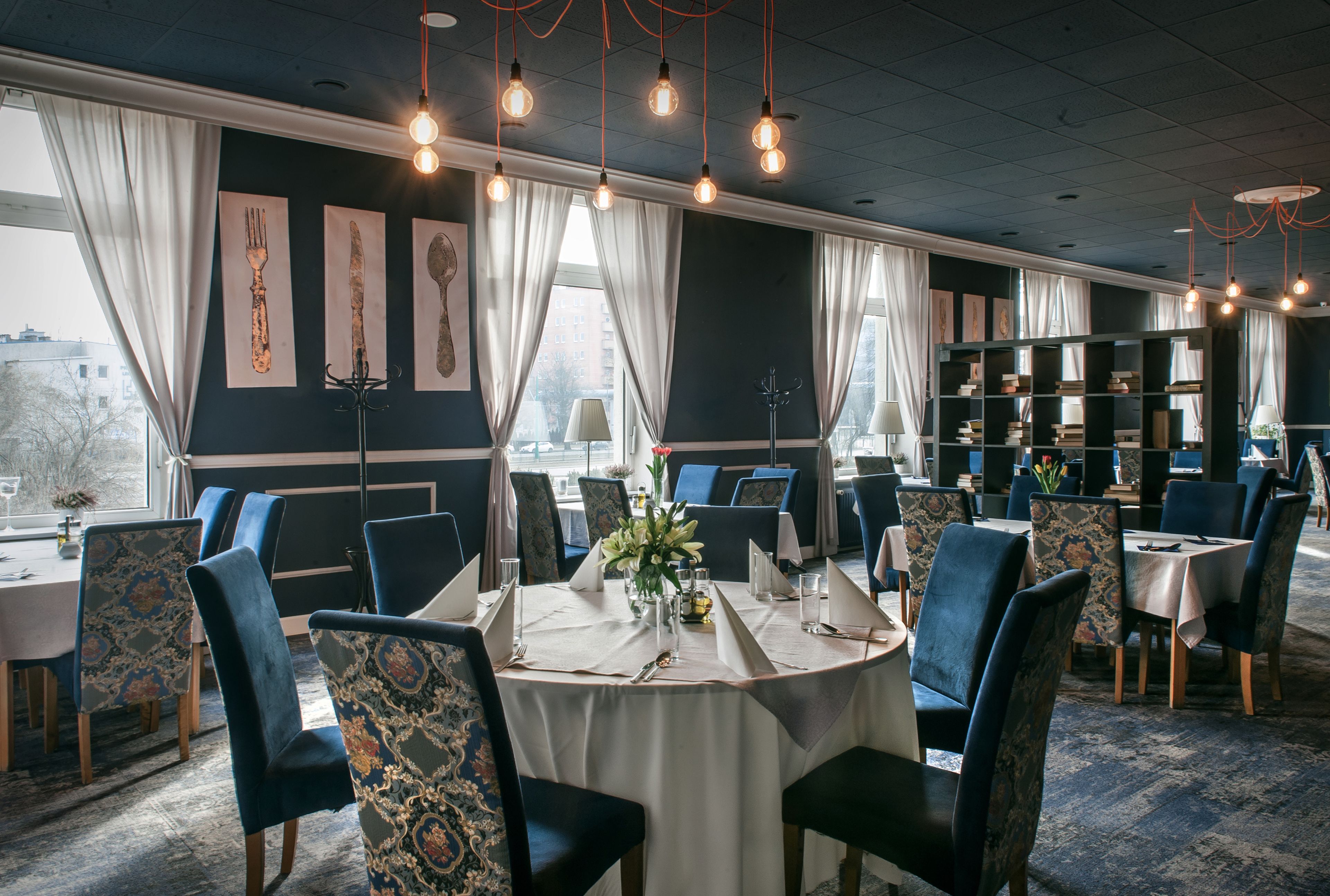 Un espace repas avec des tables rondes, des chaises à revêtement bleu et une bibliothèque en arrière-plan.