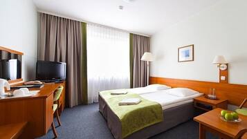 A hotel room with a bed, desk, television, and a window with curtains.