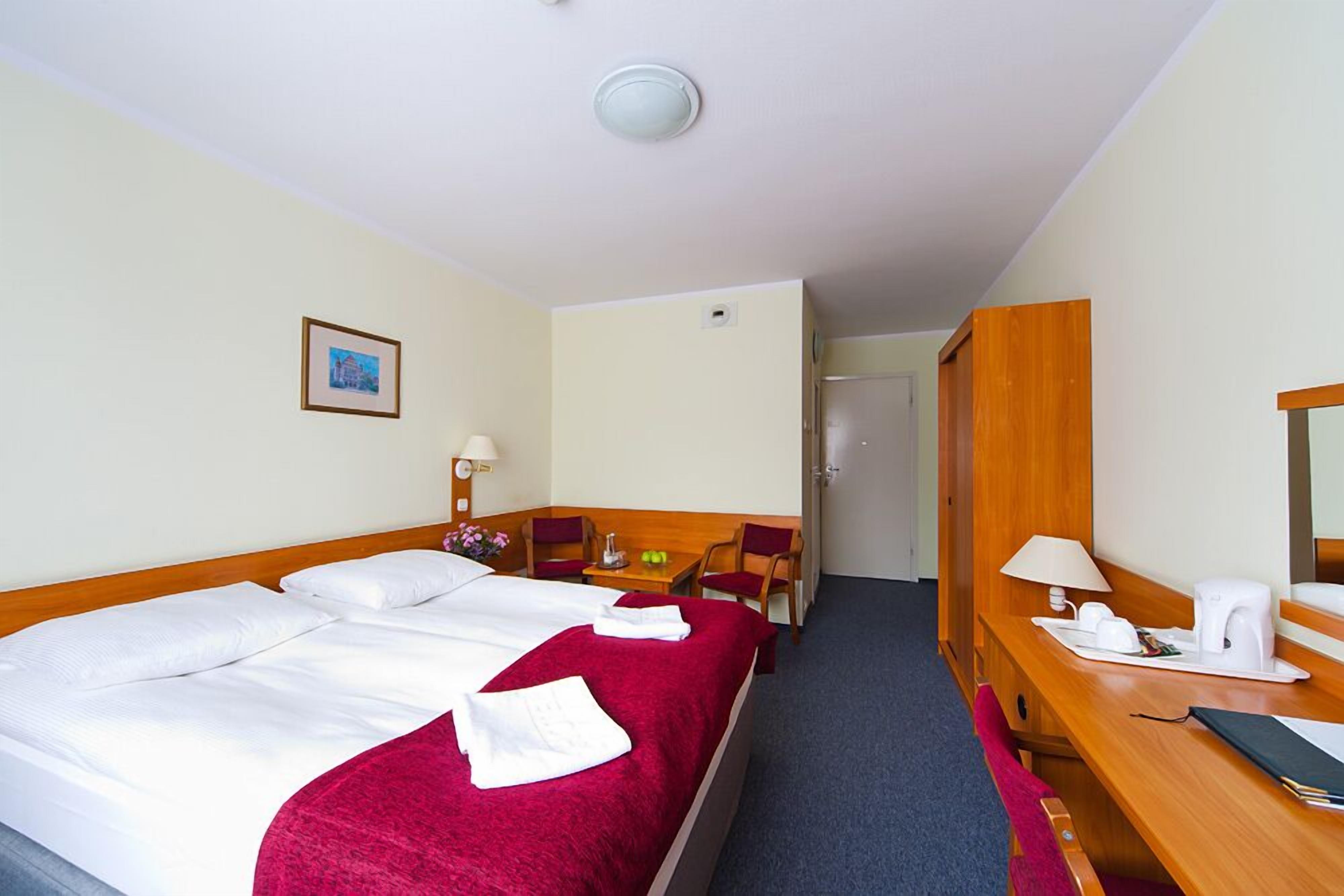 Une chambre d’hôtel avec un lit, un bureau, une chaise, une lampe et un miroir.