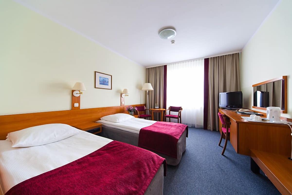 A hotel room with two beds, a desk with a chair, a television, and a window with curtains.