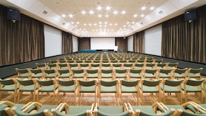 Un salón de conferencias con filas de sillas verdes y una pantalla grande al frente.