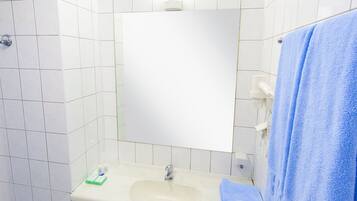 Un bagno con pareti piastrellate di bianco, un lavandino, uno specchio e un asciugamano blu appeso al muro.