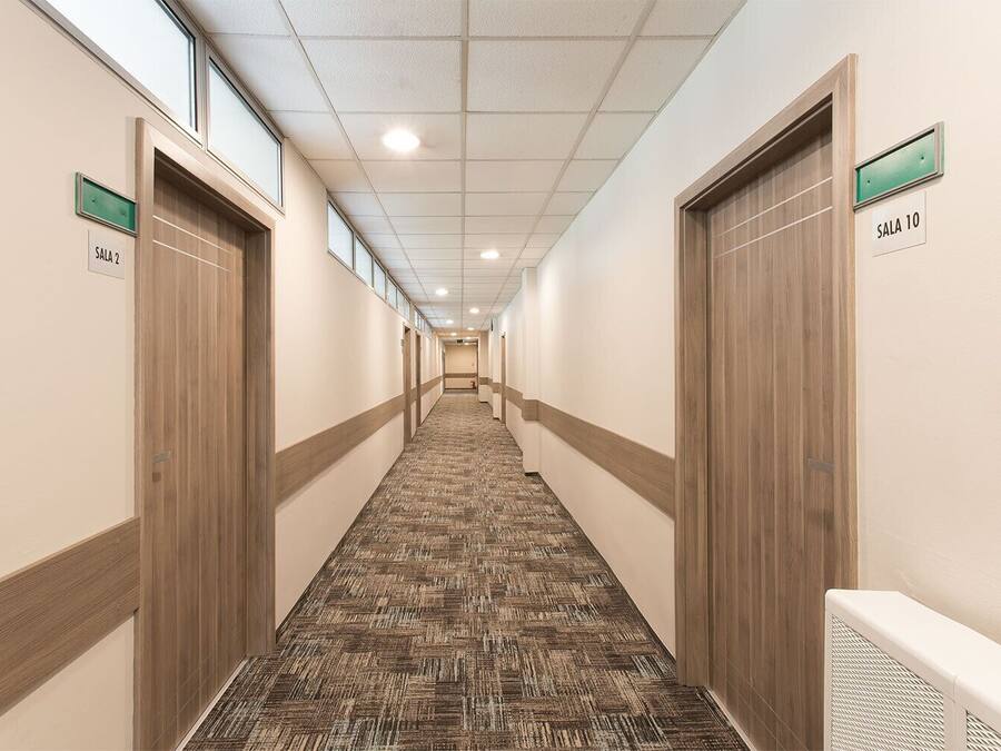 A hotel hallway with carpeted floors, wooden doors, and signs indicating room numbers.