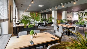 Una sala de conferencias moderna con una mesa de madera, sillas grises y plantas en macetas.