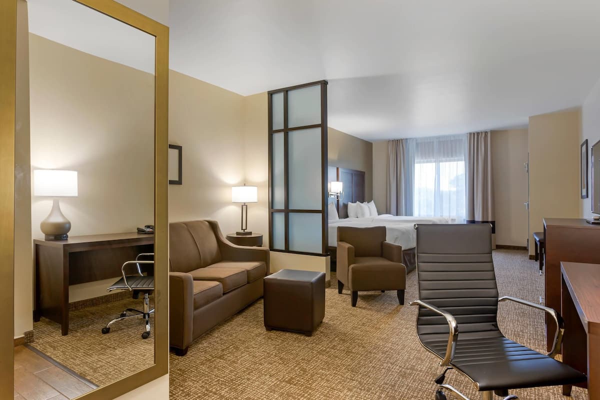 A hotel room with a large bed, a sitting area with a sofa and armchairs, a desk, and a mirror.
