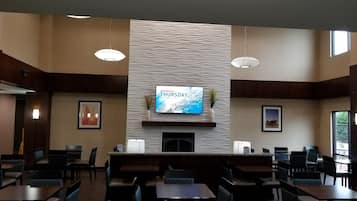Un restaurante con una televisión de pantalla plana mostrando la fecha, una chimenea y varias mesas y sillas.