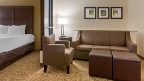 A hotel room with a bed, a sofa, a chair, a lamp, and three framed pictures on the wall. - Comfort Suites Little Rock West (Little Rock)