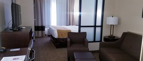 Habitación de hotel con cama, televisor, escritorio, silla, sofá y lámpara.