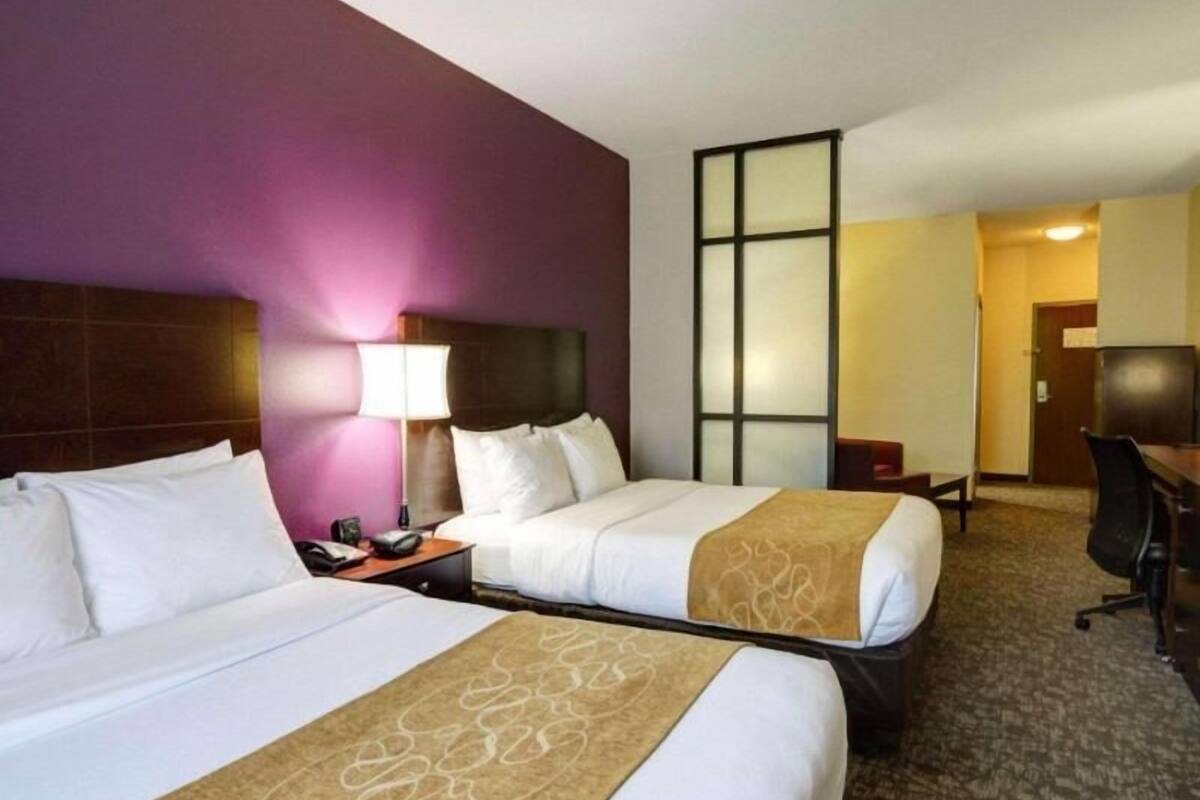 A hotel room with two beds, a desk, a chair, and a large window.