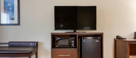 A hotel room with a flat-screen TV, a microwave, a mini-fridge, a sofa, and a small table.