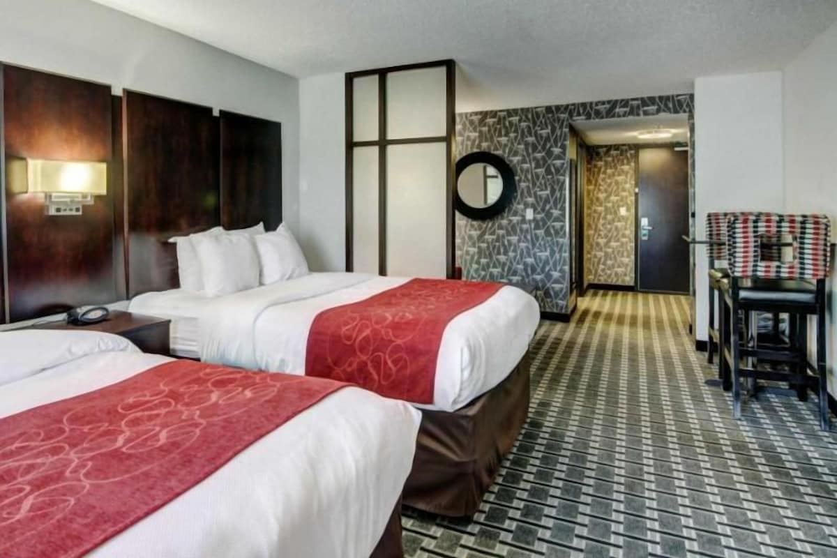 Habitación de hotel con dos camas, un escritorio, una silla, un espejo y piso con diseño.