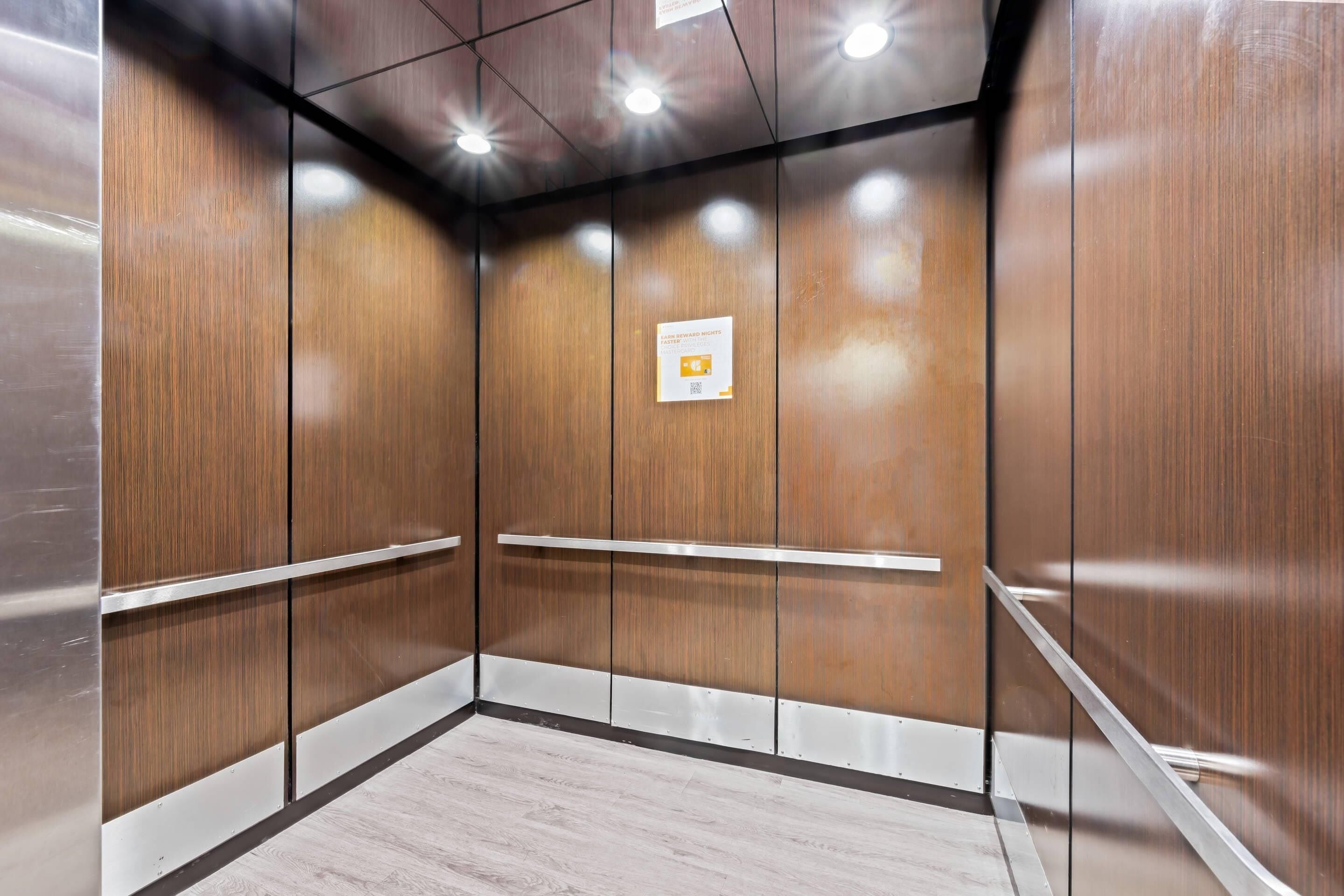 An elevator interior with wooden walls, metal handrails, and a sign on the wall.